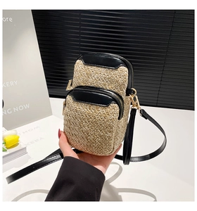 Detail of woven straw mini bag with dual zipper compartments and black faux leather trim