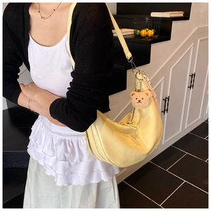 Detail of pale yellow hobo bag with crocodile texture and cute plush bear charm