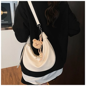 Detail of white crocodile embossed dumpling bag featuring a cute plush bear pendant accessory