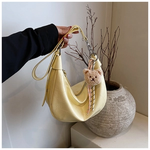 Detail of yellow hobo bag with crocodile pattern and a cute brown plush bear charm