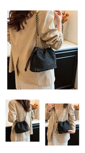 Detail of black pleated bucket bag with gold chain strap and drawstring closure