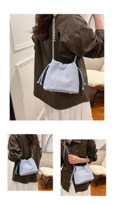 Detail view of light blue drawstring bucket bag with golden chain strap and metal feet