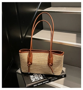 Close-up of woven straw tote bag with brown leather handles and natural texture detail