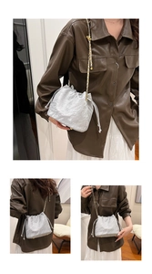 Detailed close-up of silver wrinkled texture bucket bag with chain strap and gold buckle
