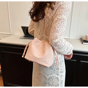 Detail of a pink drawstring bucket bag with gold chain strap on a lace dress