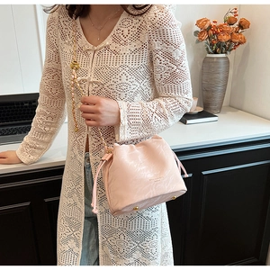 Pink drawstring bucket bag with shiny wrinkled texture and gold chain strap on model