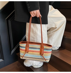 Detail of the colorful striped woven tote bag with brown leather handles on dark stairs
