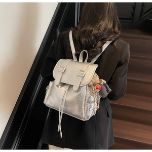 Détail d'un sac à dos argenté métallisé avec texture plissée, boucles et un charmant ours