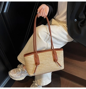Detail view of woven straw tote bag with brown leather handles and knot details