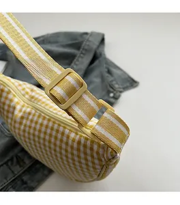Close-up of yellow checkered crescent bag with striped strap and adjustable buckle detail