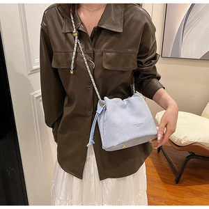Detail of light blue bucket bag featuring gold chain strap and adjustable metal bead buckle