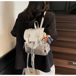 Détail d'un sac à dos argenté métallisé avec rabat à deux boucles et pendentif ours