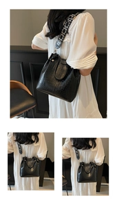 Detail of black crocodile texture bucket bag with patterned wide shoulder strap and gold hardware