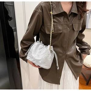 Detail of silver crinkle bucket bag with pearl chain strap worn on a leather shirt
