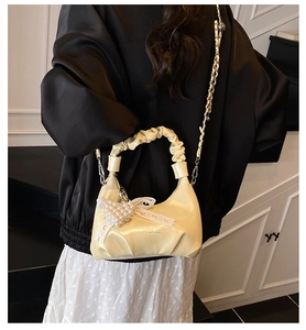 Detail of creamy yellow pleated dumpling bag with pearl bow and metal chain strap