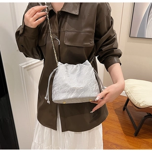 Detail view of silver drawstring bucket bag with pleated texture and bottom studs