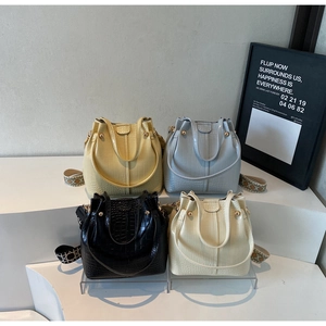 Close-up of four crocodile textured bucket bags in yellow, blue, black, and beige with wide straps