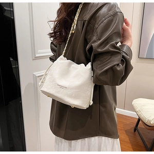 Detail view of cream bucket bag featuring textured leather and golden chain strap on model