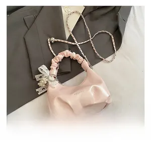 Detail of light pink pleated handbag featuring lace bow and pearl charm with chain strap