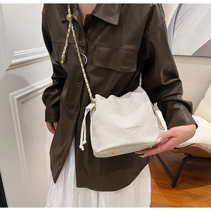 Detail shot of the white pleated bucket bag with metal chain strap and luxury branding