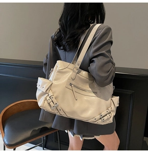 Detail of a beige large tote bag with moto-style straps and rivets worn by a model