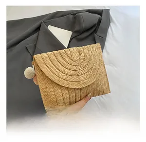 Détails d'un sac enveloppe en paille tressée à la main avec pompon décoratif latéral