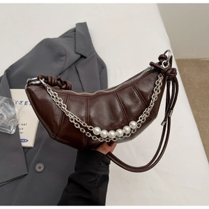 Detail of dark brown croissant bag featuring quilted texture, pearls, and silver chain strap