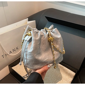 Detail of silver drawstring bucket bag with metallic texture and gold chain strap