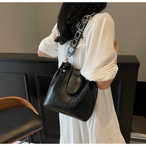 Model wearing a black crocodile embossed bucket bag with a geometric wide strap and lace dress