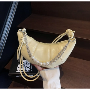 Detail of beige croissant bag featuring silver chains, pearls and leather knot straps