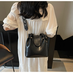 Detail of black crocodile texture bucket bag with geometric embroidered wide strap