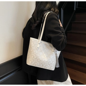 Dettaglio della borsa tote beige con motivo geometrico e nappa grigia sulla spalla