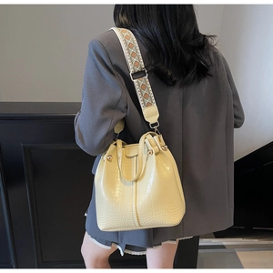 Detail of light yellow bucket bag with crocodile texture and ethnic embroidered strap