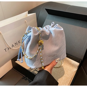 Close-up of light blue drawstring bucket bag with gold chain strap and metal pendant