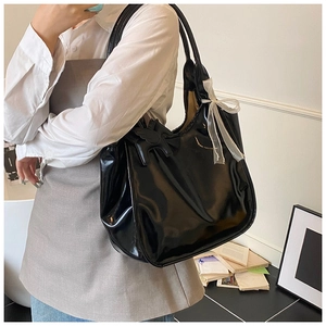 Close-up of black glossy patent leather tote bag with lace bow and horse charm