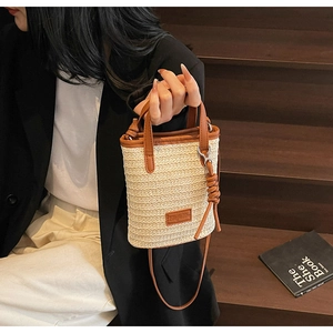 Detail of woven straw mini bucket bag with brown leather trim and shoulder strap