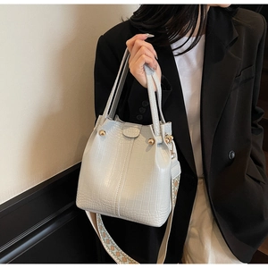 Detail of grey crocodile embossed bucket bag with gold studs and woven strap