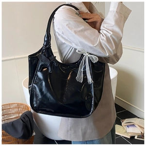 Detail of glossy black tote bag featuring a pegasus charm and delicate mesh bow ornament