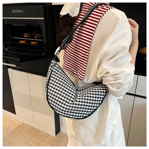 Detail of black and white gingham crescent bag worn over the shoulder in a cozy kitchen
