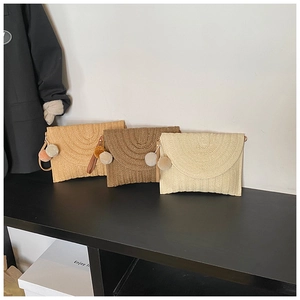 Détail de pochettes en paille tressée en trois couleurs avec breloques pompons en peluche