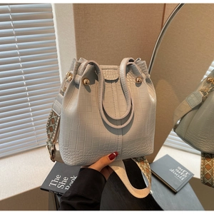 Close-up of light blue bucket bag with crocodile texture and woven wide strap