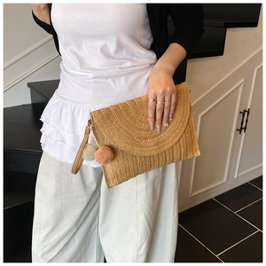 Détail d'une pochette en paille tressée avec pompons colorés et dragonne pour le poignet
