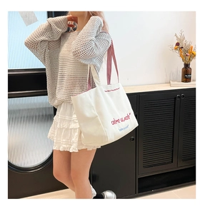 Détail du sac cabas en toile avec texte brodé et bandoulières à rayures rouges