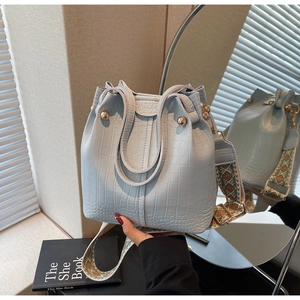 Detail of light blue croc-effect bucket bag with round handles and wide woven strap