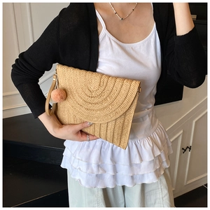 Détail d'une pochette en paille tressée avec textures superposées et pompon rose