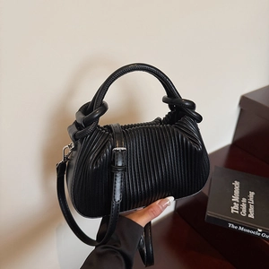 Detail of black pleated faux leather handbag with knotted handle and adjustable strap