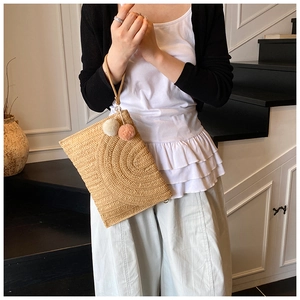 Détail d'une pochette en paille tressée avec pompons décoratifs et dragonne pratique