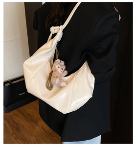 Detail view of glossy cream hobo bag with pink plush bear charm and sleek patent leather