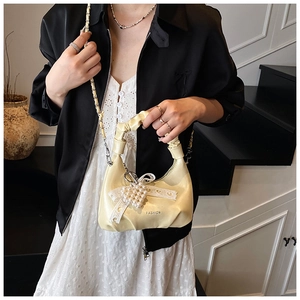 Detail of cream pleated handbag with pearl charms, lace bow, and metal chain strap