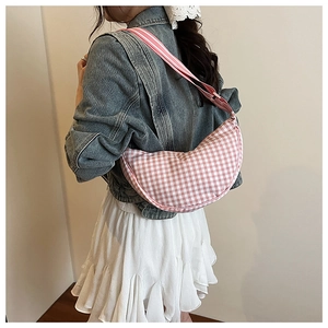 Detail of pink plaid crescent bag with adjustable striped strap worn on the shoulder